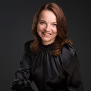 Portret przedstawia Joannę Solecką jako uśmiechnietą kobietę w czarnej bluzce