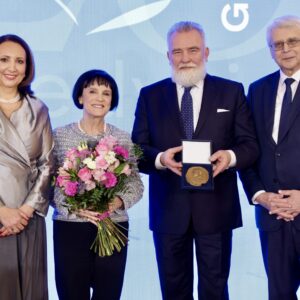 dwie elegancko ubrane kobiety, jedna z nich trzyma bukiet kwiatów, stoją obok dwóch elegancko ubranych mężczyzn, jeden z nich trzyma nagrodę w postaci medalu w futerale