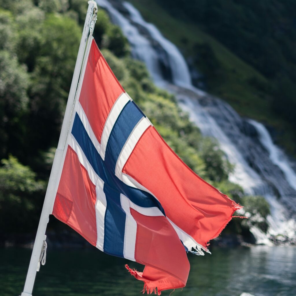 powiewająca flaga Norwegii na tle zbocza góry i wodospadu