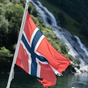 powiewająca flaga Norwegii na tle zbocza góry i wodospadu