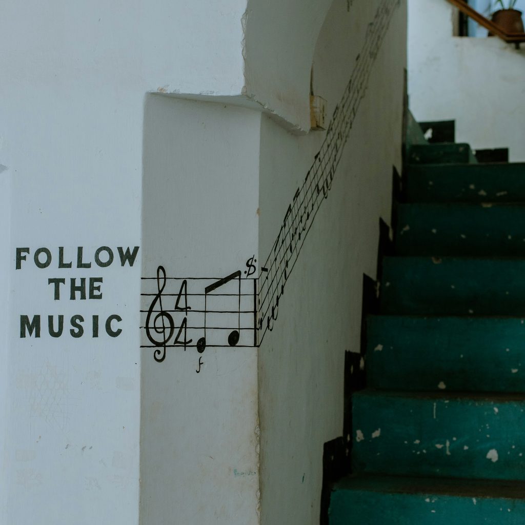 na białej ścianie namalowany napisa Follow the Music i nuty, a obok zielone schody na klatce schodowej
