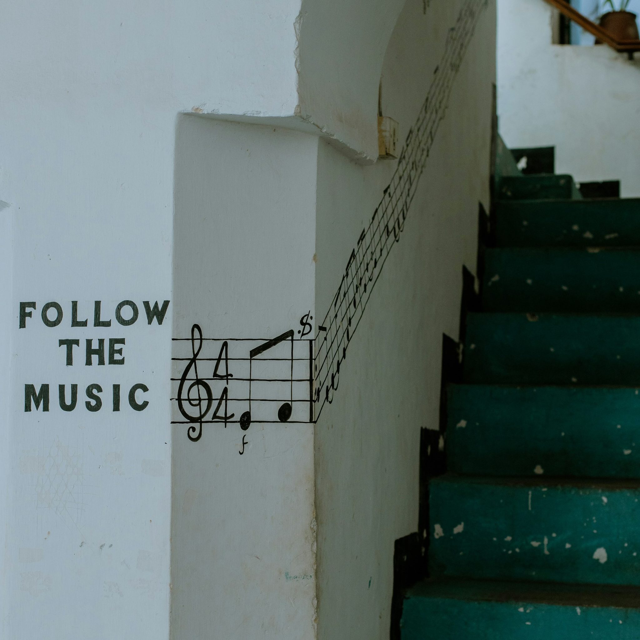 na białej ścianie namalowany napisa Follow the Music i nuty, a obok zielone schody na klatce schodowej