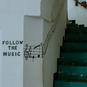 na białej ścianie namalowany napisa Follow the Music i nuty, a obok zielone schody na klatce schodowej