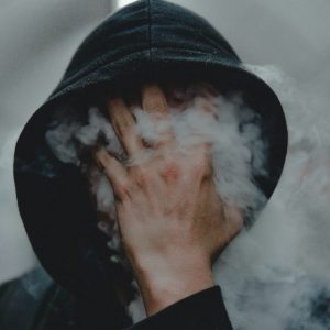 głowa osłonięta kapturem, ręka dotyka zadymioną twarz