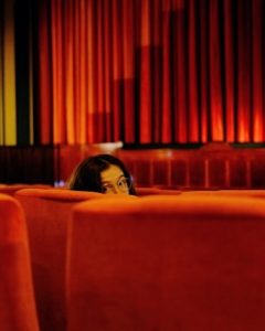 Kobieta siedząca w fotelu w teatrze operowym, zerkająca przez ramię w stronę obiektywu.