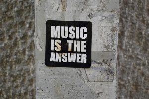 Naklejka z napisem "Music is the answer" umieszczona na szarym tle budynku.