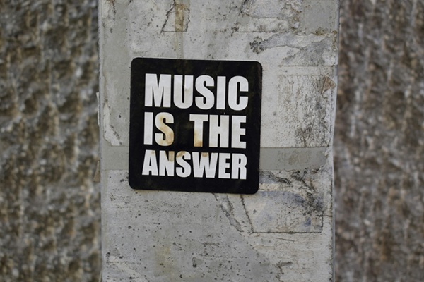 Naklejka z napisem "Music is the answer" umieszczona na szarym tle budynku.