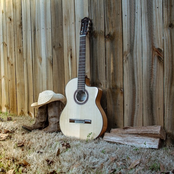 gitara stoi oparta o stodołę, obok leżą buty kowbojskie, kapelusz i kawałki drewna